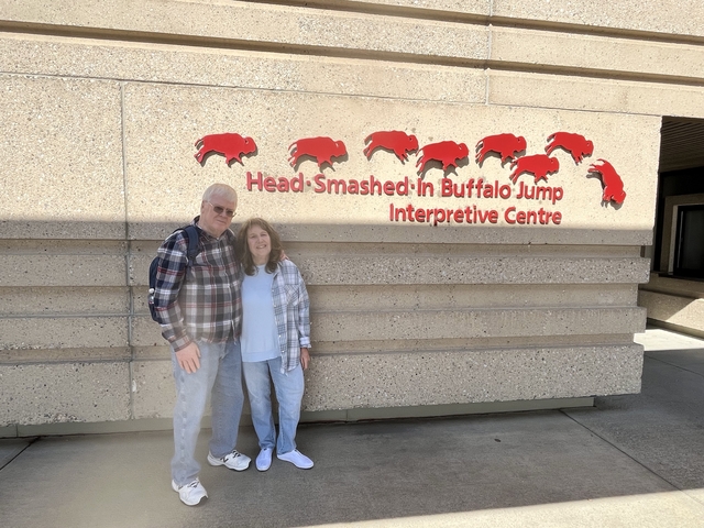 Two people posing outside the Head-Smashed-In Buffalo Jump Interpretive Centre.