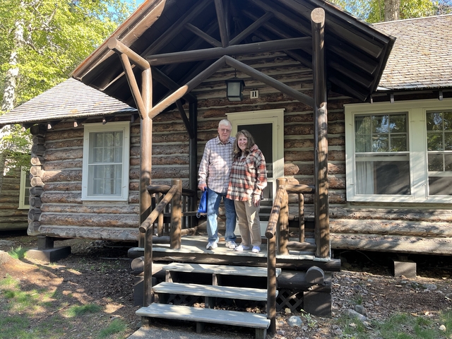       A couple standing in front of a rustic log cabin.
  