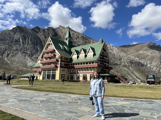 A person standing in front of the iconic Prince of Wales Hotel with mountains in the background.
