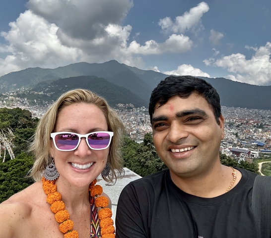       Close-up of two people posing with a city and mountains in the background.
  