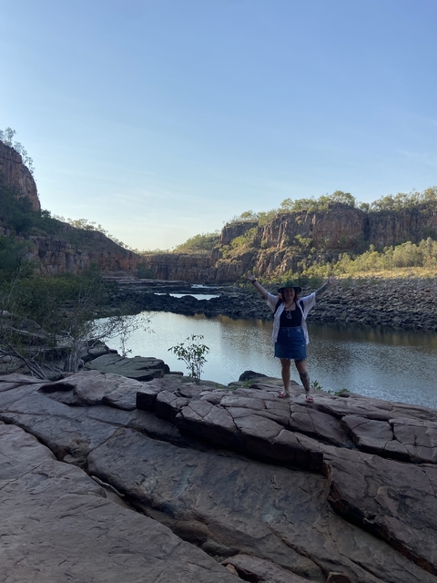 Person posing in front of a scenic canyon with a water body.