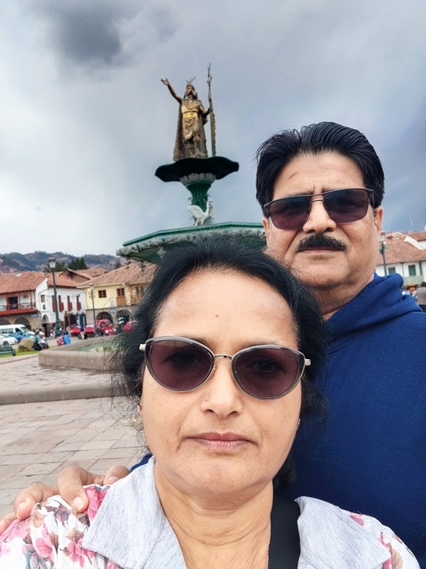 Close-up of two people with a fountain and buildings in the background.