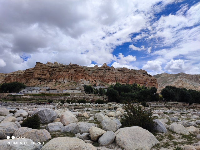       Rocky cliff with buildings at the base and a blue sky.
  