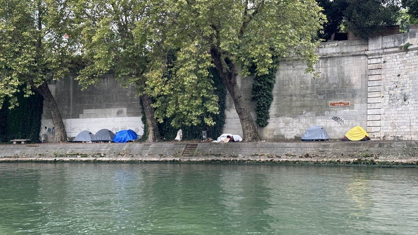       Row of colorful tents along a riverbank with trees.
  