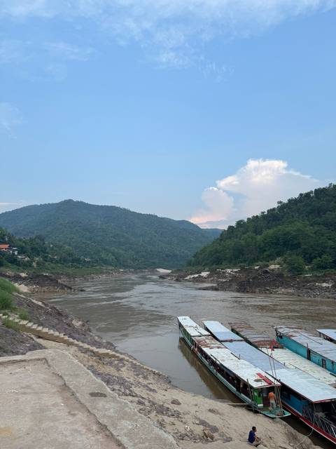 Boats docked along a river with hilly backdrop.