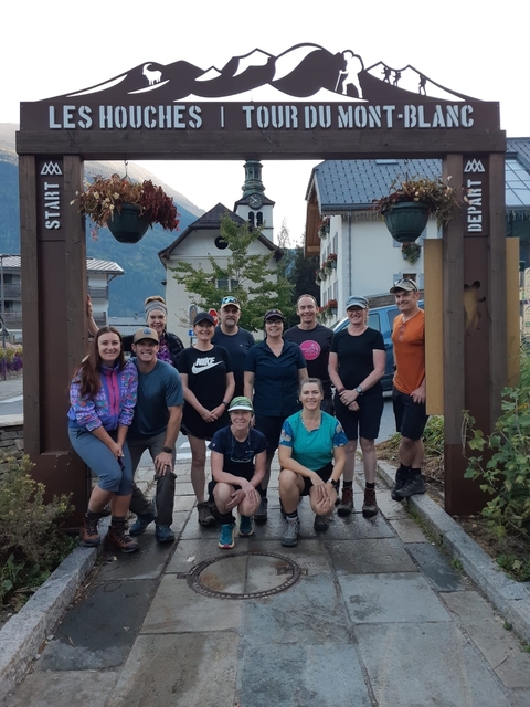 Group of people posing under a wooden archway.