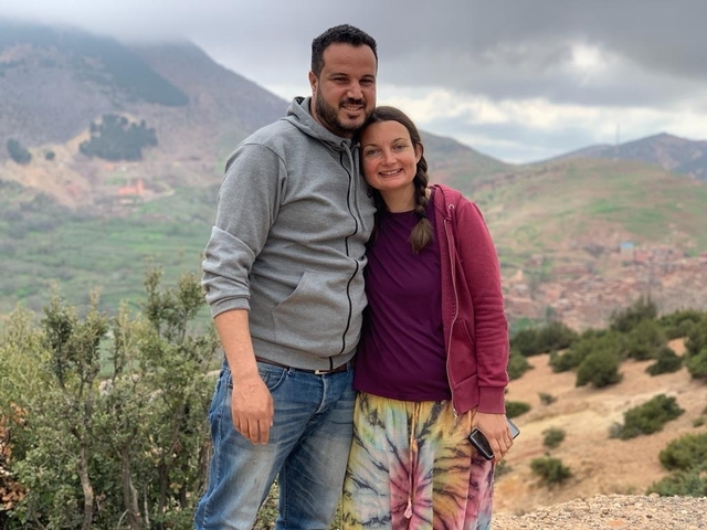       A couple posing on a hill with a village in the background.
  