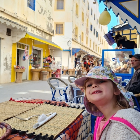       A child sitting at a marketplace with colorful shops in the background.
  