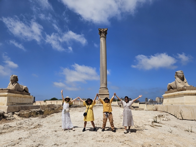 A group posing with arms raised at the Pompey's Pillar in Egypt.