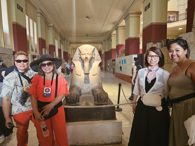 A group of tourists standing in front of a Sphinx statue inside a museum.