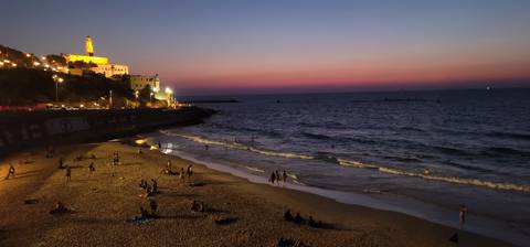       A beach at sunset with a lit-up tower in the background.
  