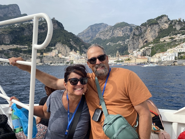A couple smiling on a boat with the Amalfi Coast in the background.