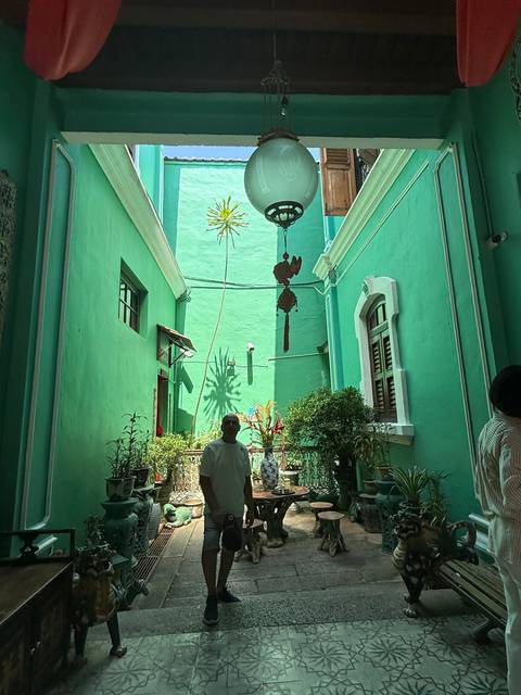 Man walking in a courtyard with green walls and tropical plants.