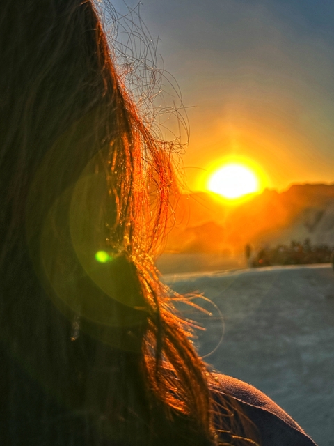       Close-up of a person with a sunset and landscape in the background.
  