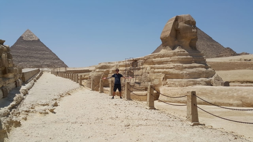       Person posing with arms stretched out in front of the Sphinx and Pyramid of Giza.
  