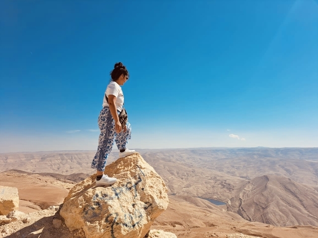 Person standing on a rocky outcrop overlooking a vast desert landscape.