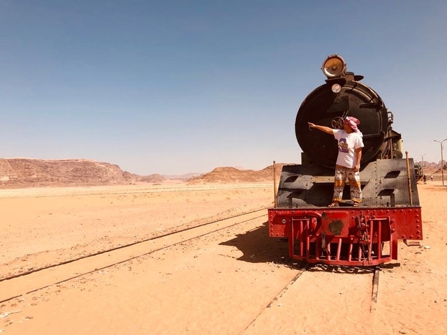Person standing on a train at a desert location with tracks.
