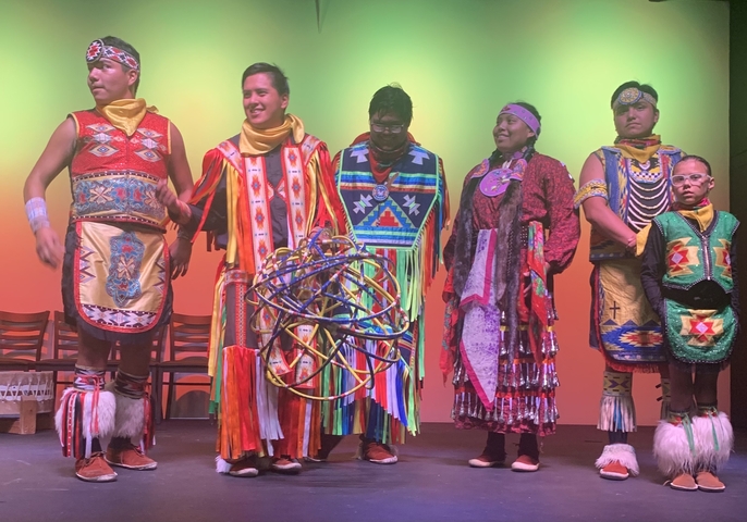A group of people dressed in traditional Native American attire on a stage.
