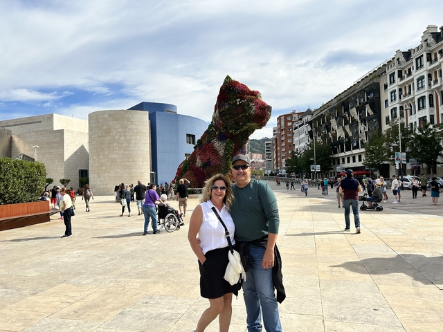 A couple posing in front of a large flower dog sculpture in a city square.
