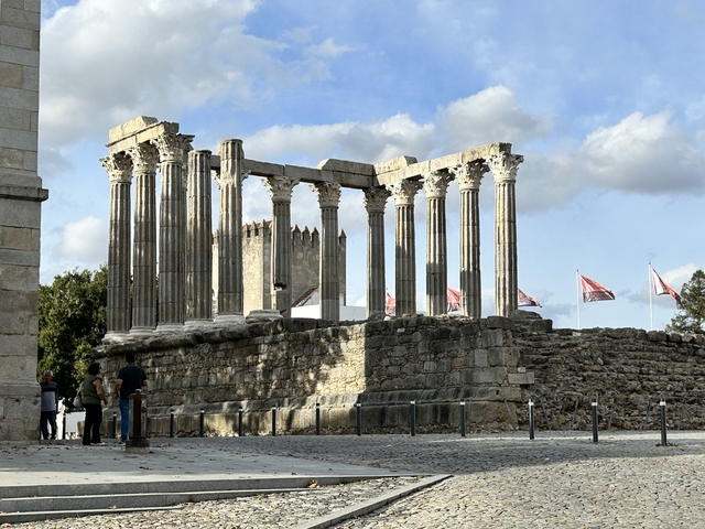       Roman-style temple ruins with columns under a cloudy sky.
  