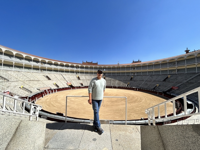       Person standing inside a large bullring.
  