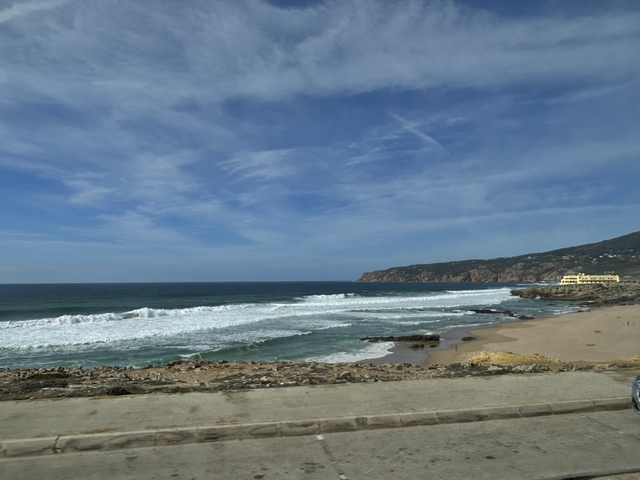       Coastal scene with waves breaking on the shore under a cloudy sky.
  