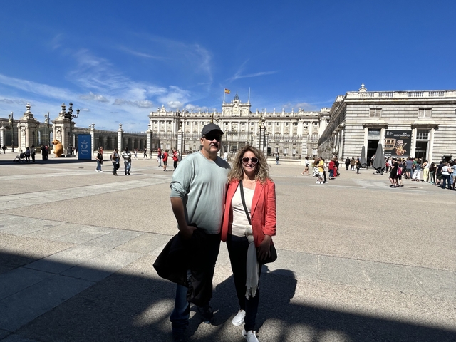       A couple posing in front of a grand building under a clear sky.
  