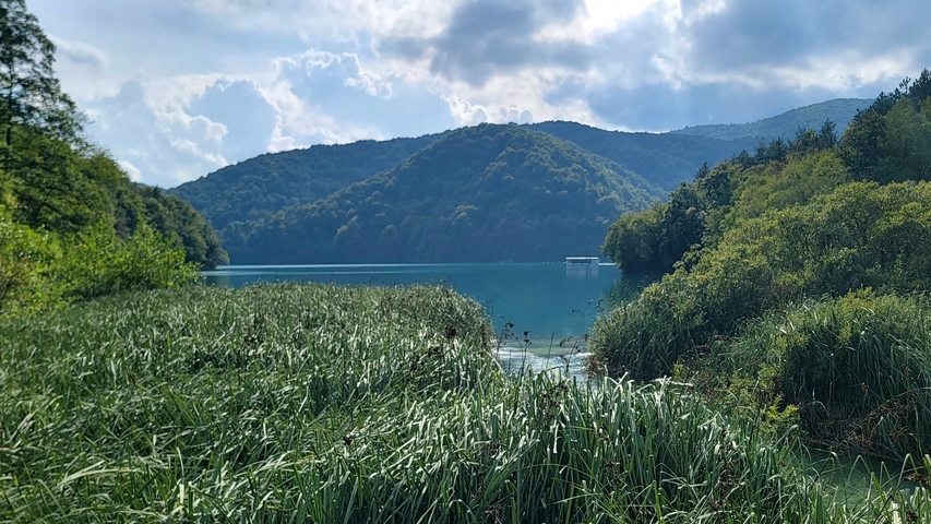 Lake surrounded by lush greenery and distant hills.