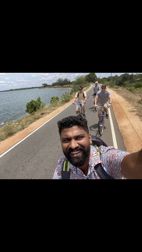 Group of people cycling on a rural road beside a body of water.
