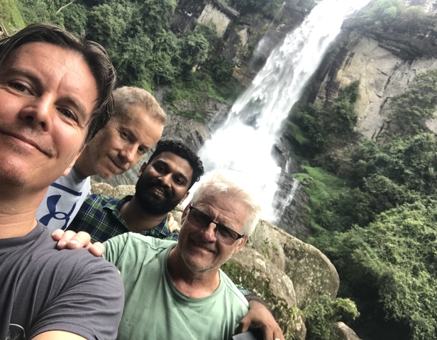 Four men posing in front of a waterfall.
