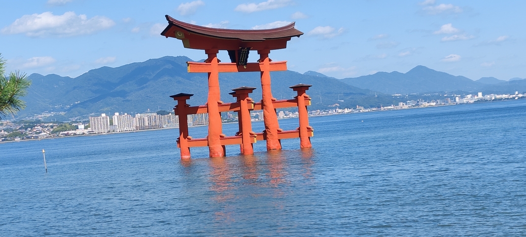 Iconic red torii gate standing in water with mountains in the background.