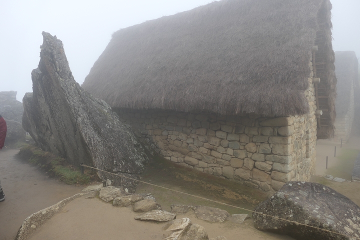      Ancient stone building with thatched roof in foggy conditions.
  