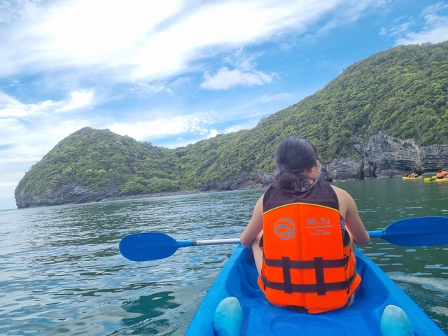 A person kayaking on a serene water body surrounded by hills.