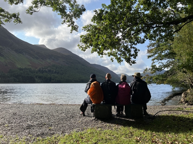 Group of people sitting by the lakeside with mountains in the background.