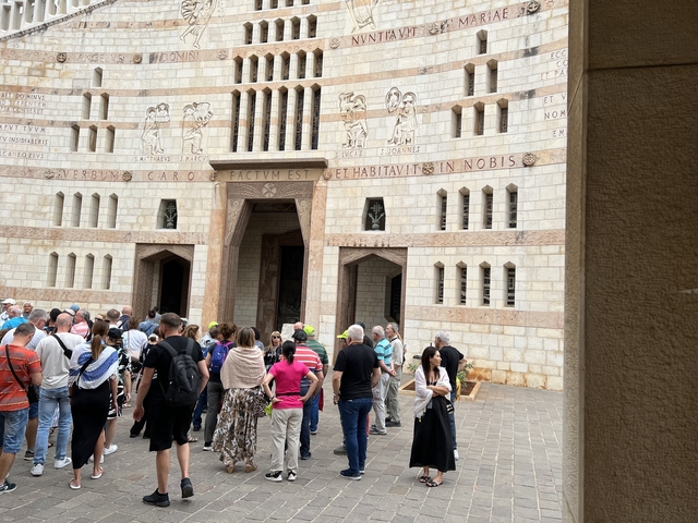       Tour group outside a large stone building with inscriptions.
  