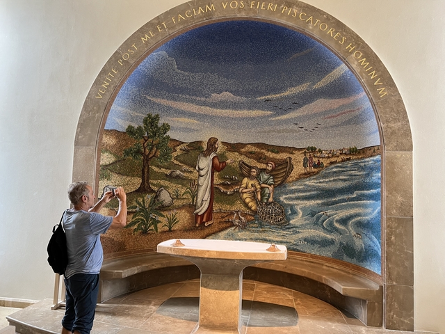       Religious mosaic in a chapel with a man taking a photo.
  