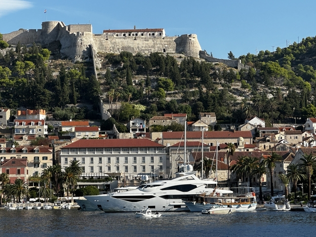A picturesque view of a yacht in front of historic buildings and a fort on Hvar Island, Croatia.