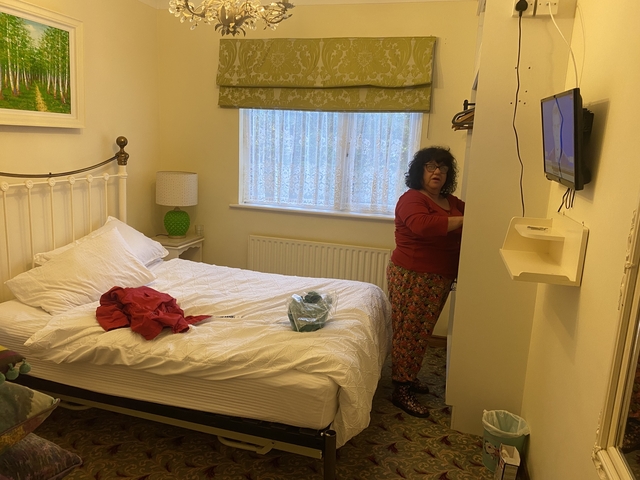 Woman in a bedroom standing beside a wardrobe.