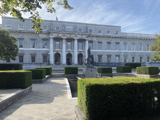       A stately neoclassical building with a bronze statue and geometric hedges in front.
  