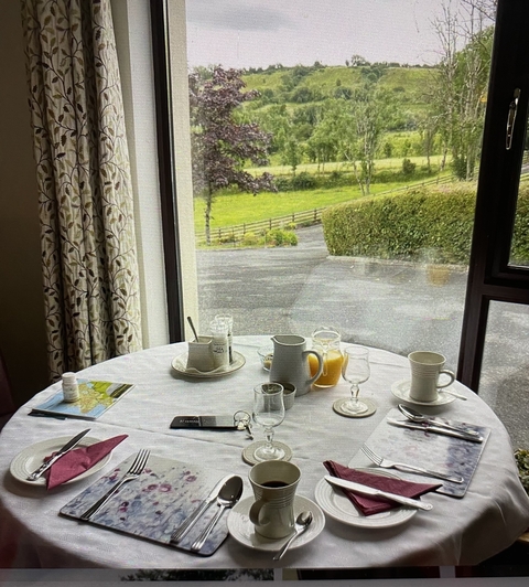 Breakfast table set with glasses and cups overlooking a garden.