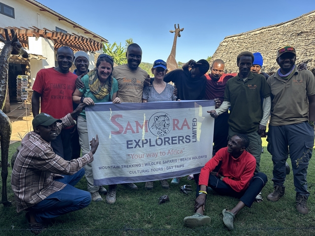 A group of people with a banner, smiling and gathered in front of a lodge.