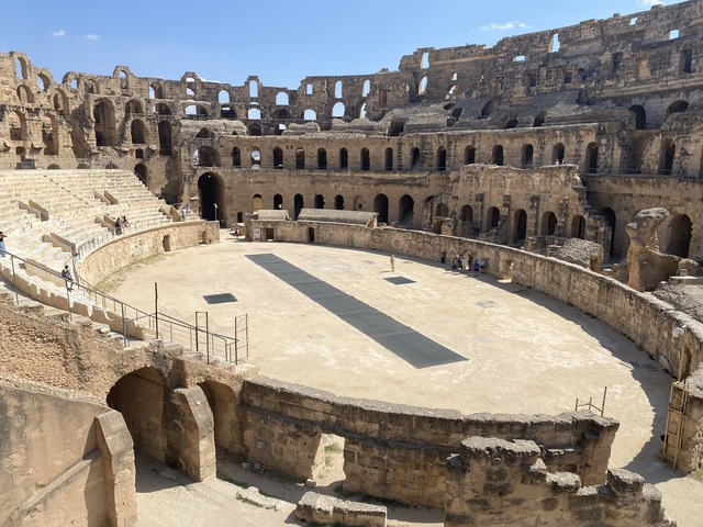       A large ancient amphitheater with tourists inside.
  