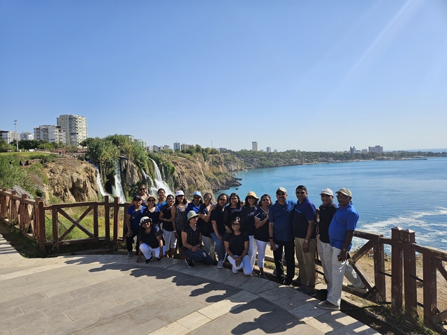       Group of people posing in front of a waterfall with a city in the background.
  