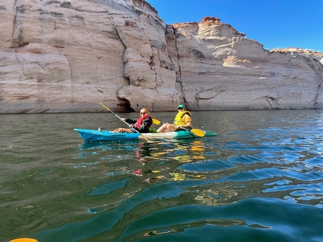 Two people kayaking on a clear blue lake surrounded by rocky cliffs.