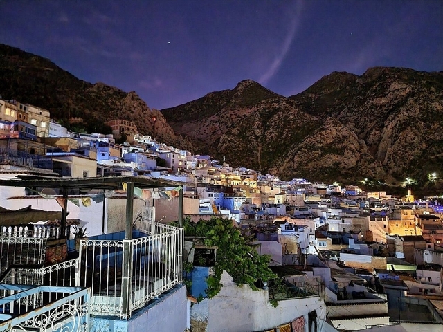 Nighttime view of Chefchaouen illuminated under mountain shadows.