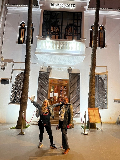 Two people posing in front of a Moroccan building entrance with palm trees.