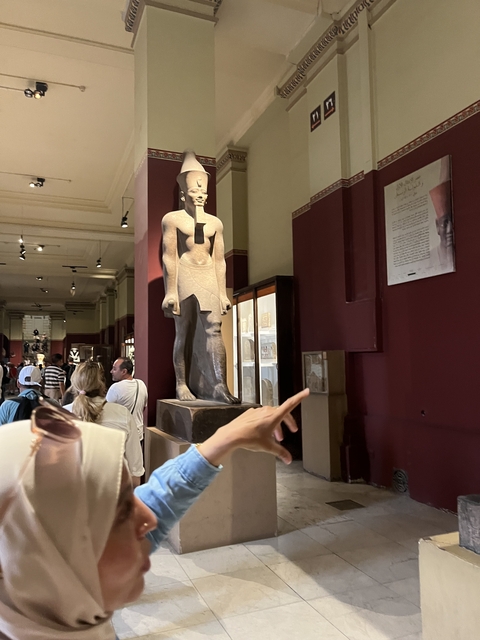       People inside a museum with a large statue in the background.
  