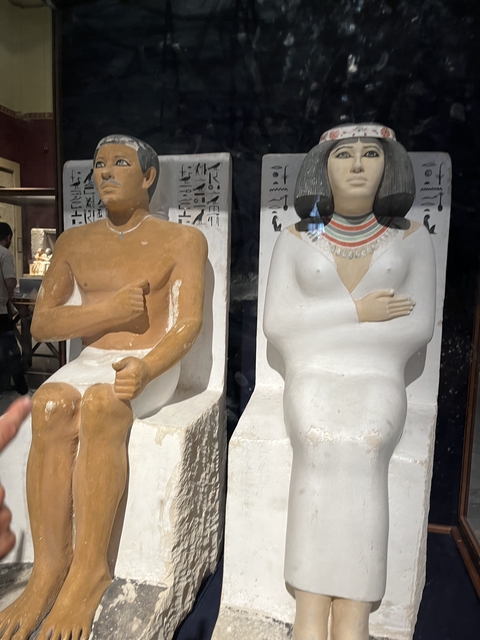       Two seated statues in a museum setting.
  