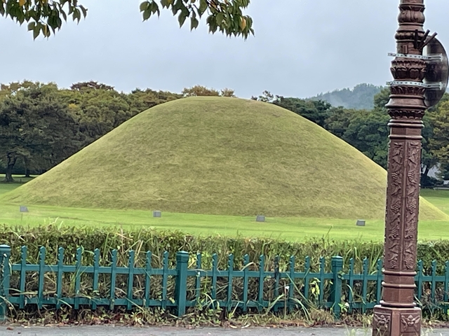 Large grass-covered burial mound surrounded by trees.