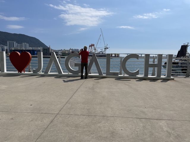 Tourist taking photo near I ❤️ Jagalchi sign by the water.